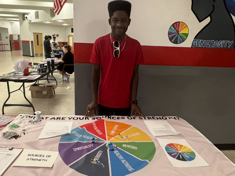 A student poses behind a "Sources of Strength" table.