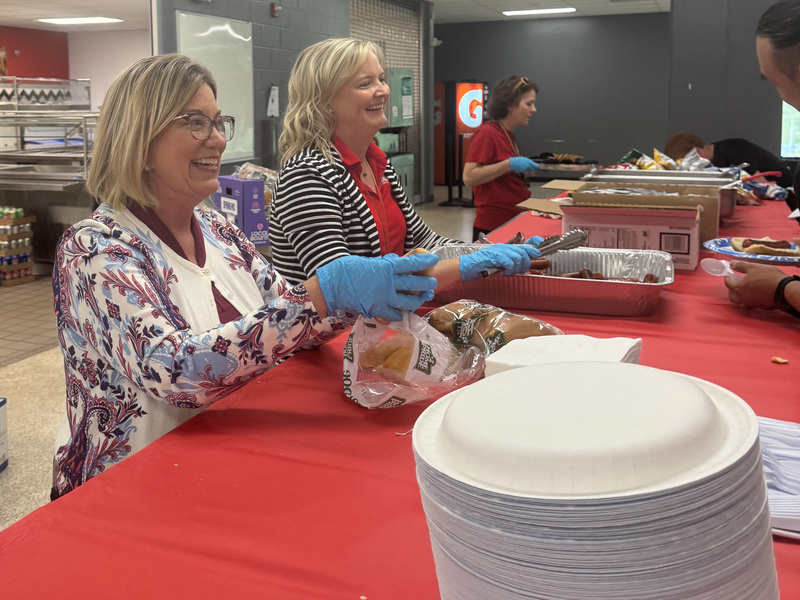 Two women serving food smile at visitors.
