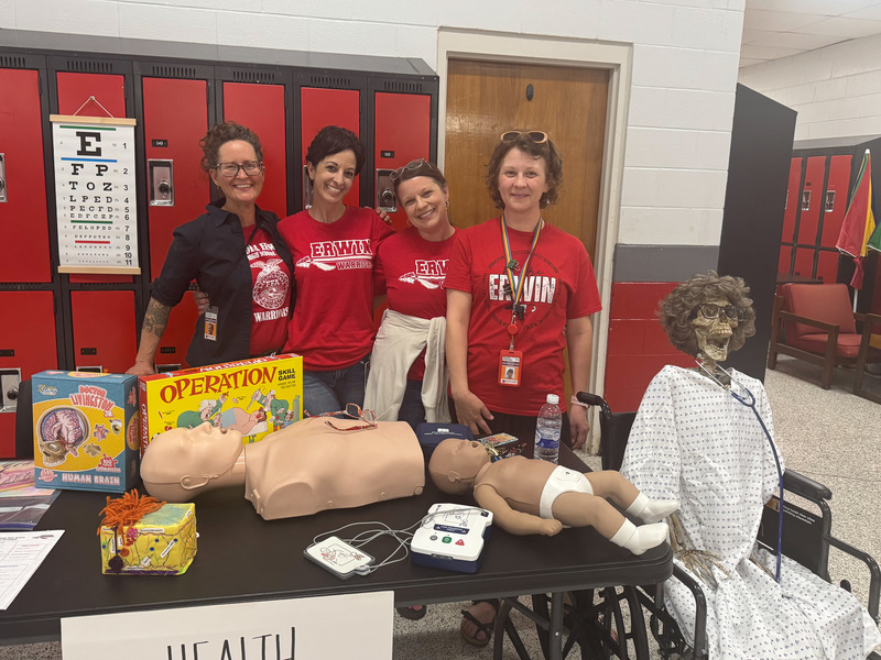 Erwin science teachers wearing red shirts stand next to a skeleton in a wheelchair.