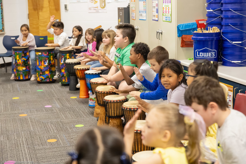 Students play hand drums in music class.