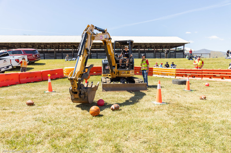 A student uses a backhoe to try to get a basketball off a traffic cone at the Haywood County Fairgrounds.