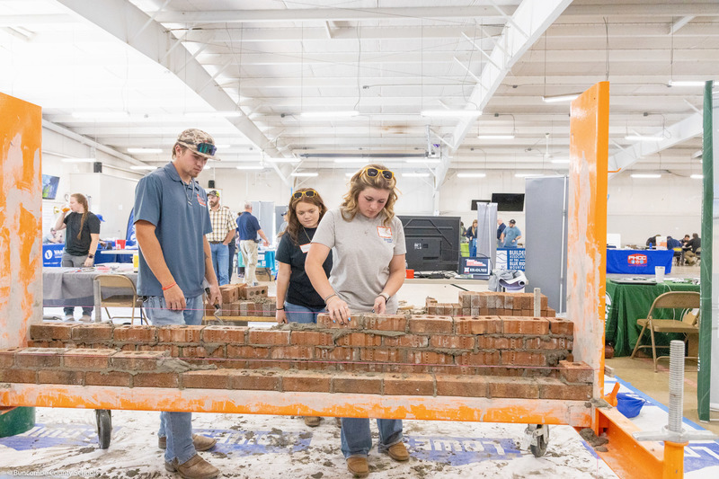 Three students practice bricklaying.
