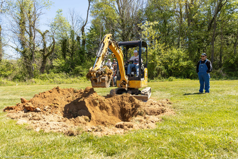 A student digs a hole with a backhoe at the fairgrounds.