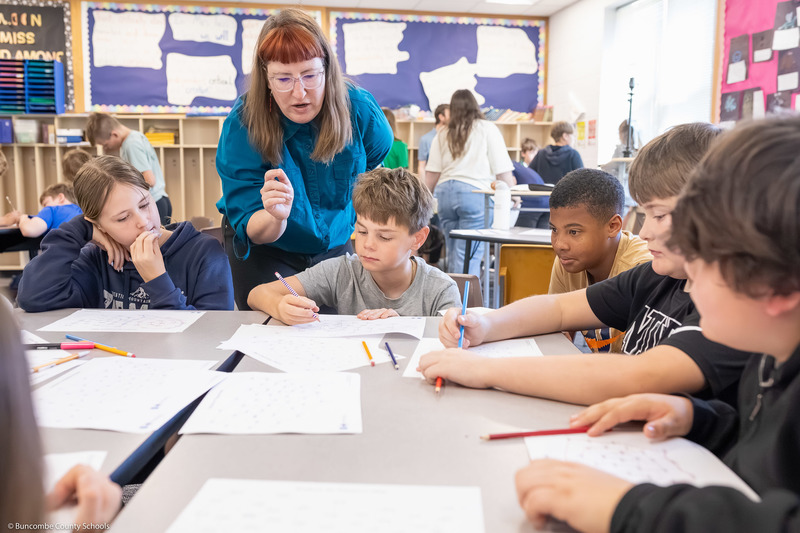 Students lean over a worksheet while one of the presenters talks to them.