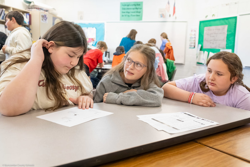 Three students lean over worksheets.