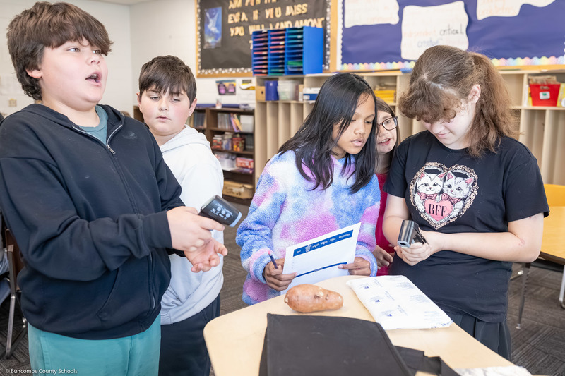 Students use an infrared thermometer to measure the temperatures of objects on a table.