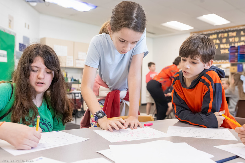 Three students lean over worksheets.