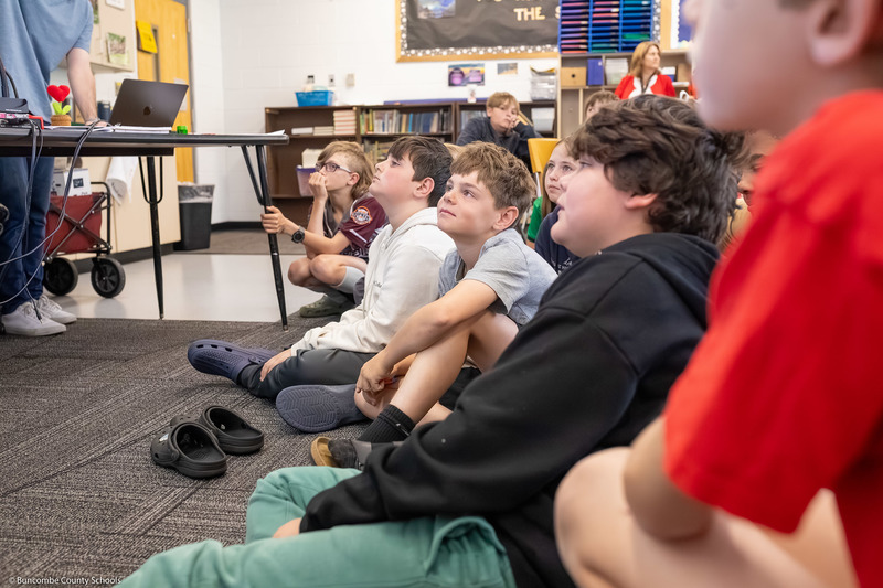 Students sit on the floor while listening to the presentation part of the program.