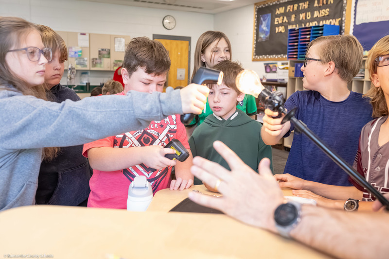 Students use an infrared thermometer to measure the temperatures of objects on a table.