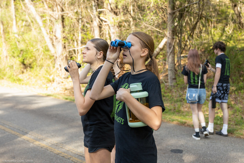 Two students hold binoculars on a trail while bird watching.