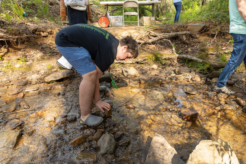 A student looks under a rock in a creek.