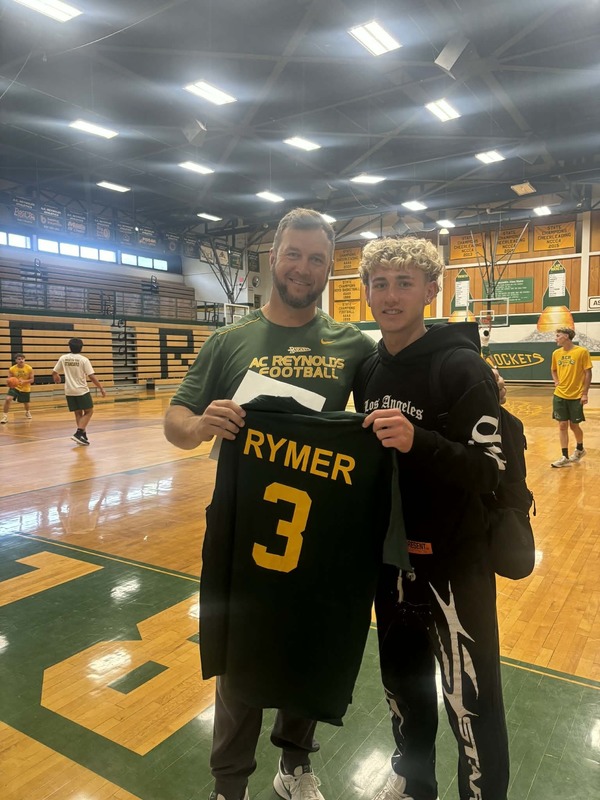 Baseball senior standing with a teacher who received his impact shirt. 