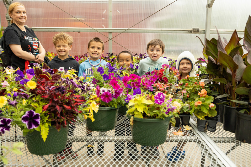 Students pose behind flowers in the greenhouse.