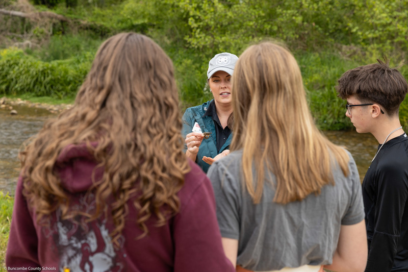 An adult shows a crayfish to three students.
