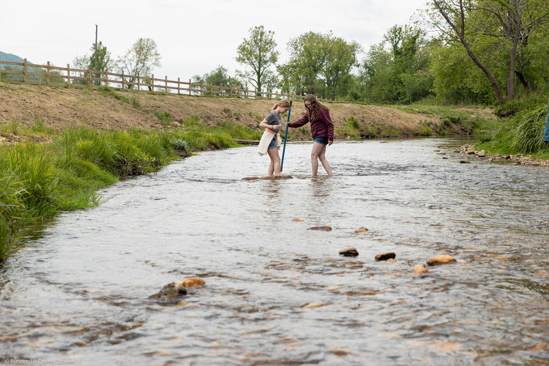 Two students look into a net while standing in the creek.