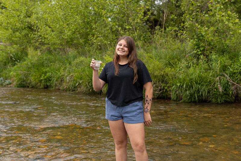 A student smiles while posing and holding a water sample.