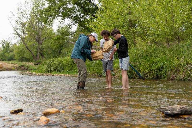 Two students and an adult look into nets while standing in the creek.