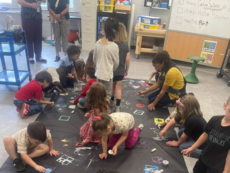Students on the floor making chalk dust color on a large piece of black fabric.
