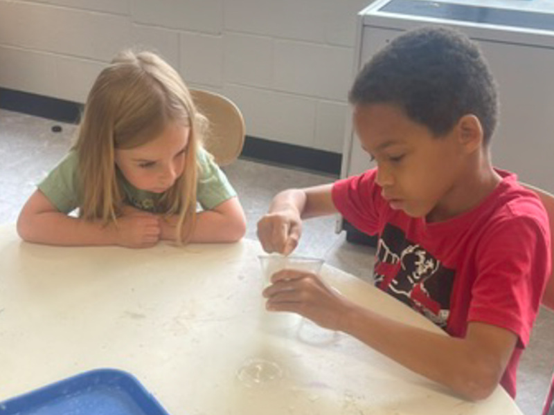 Two students sit at a table making chalk dust.