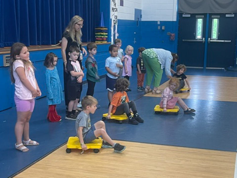 Students in the gym sit on rollie-carts.