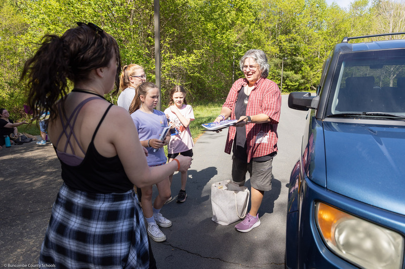 A teacher hands out books to kids.