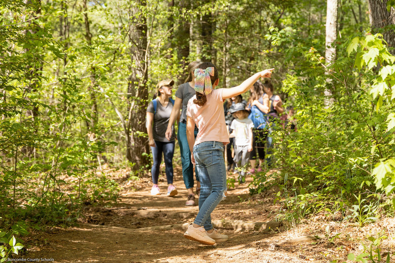 A girl points at a tree as other students come down a trail.
