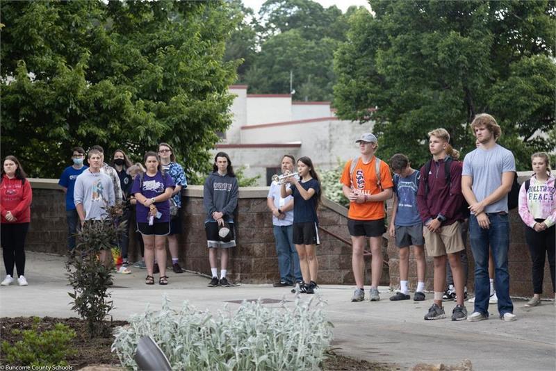 Students standing respectfully while a student plays the trumpet