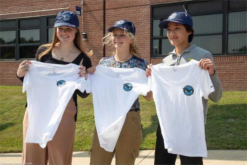 Three students holding matching t-shirts