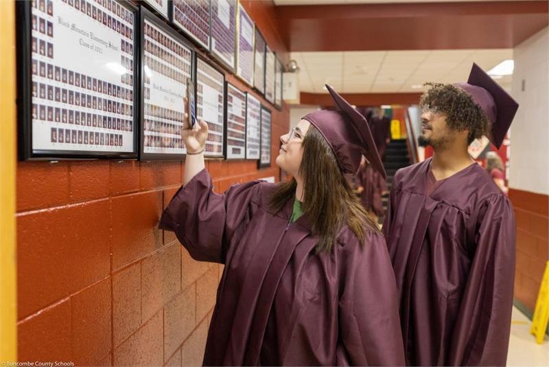 Graduates looking at graduating class pictures hanging on the wall Graduates looking at graduating class pictures hanging on the wall