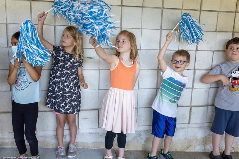 Younger students lined up along the wall holding pompoms Younger students lined up along the wall holding pompoms