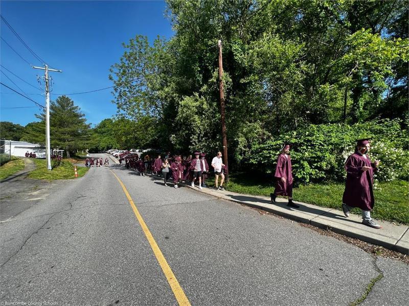 Graduates walking down the sidewalk along a street Graduates walking down the sidewalk along a street