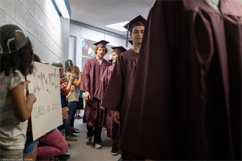 Graduates walking down the hall past younger students holding signs Graduates walking down the hall past younger students holding signs