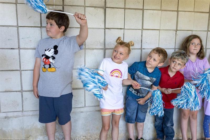 Younger students lined up along the wall holding pompoms Younger students lined up along the wall holding pompoms