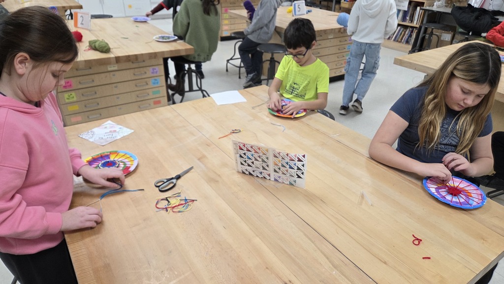 4Y students working at tables, weaving their multi-colored yarn onto a colorful circle loom.