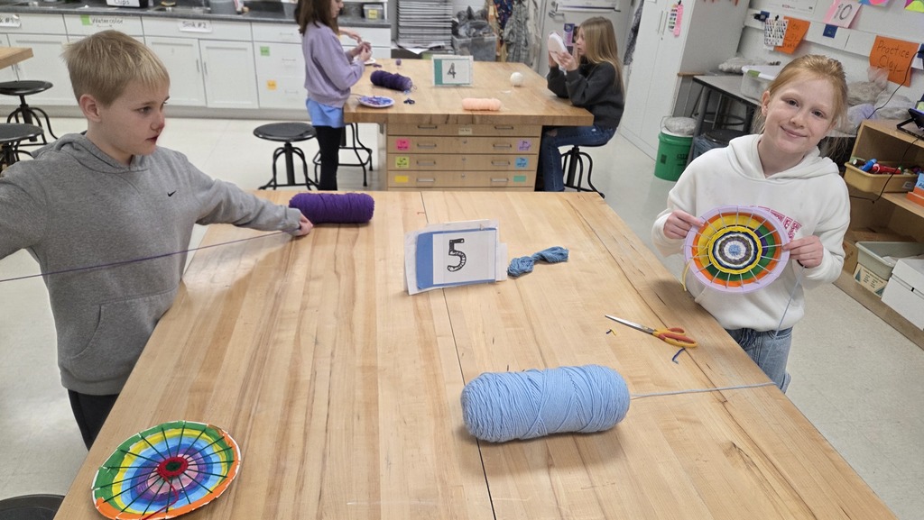 4Y students working at tables, weaving their multi-colored yarn onto a colorful circle loom.