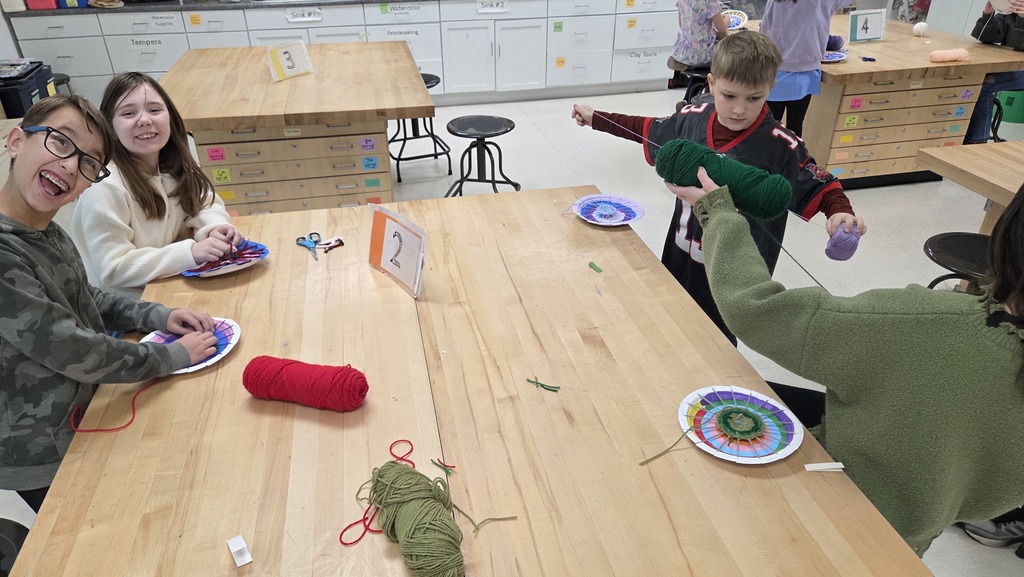 4Y students working at tables, weaving their multi-colored yarn onto a colorful circle loom.