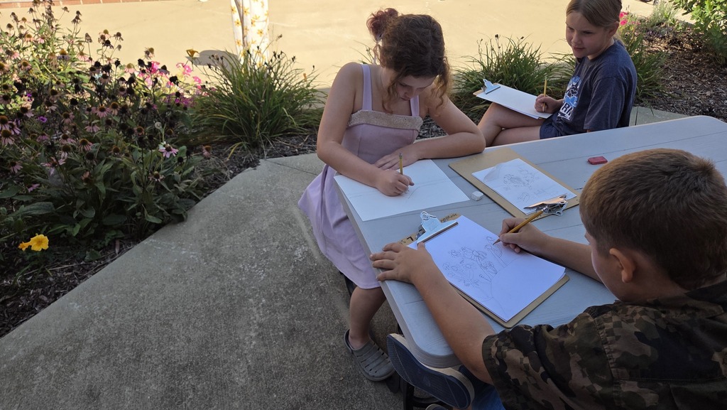 Students drawing at a table in the courtyard.