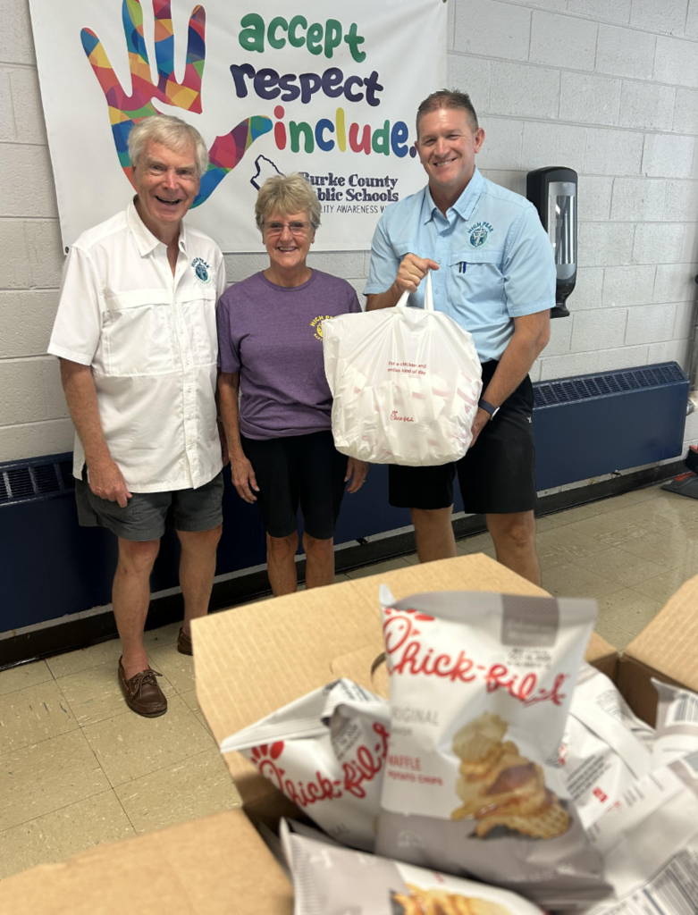 Three people standing in a cafeteria holding a Chick Filet bag. 