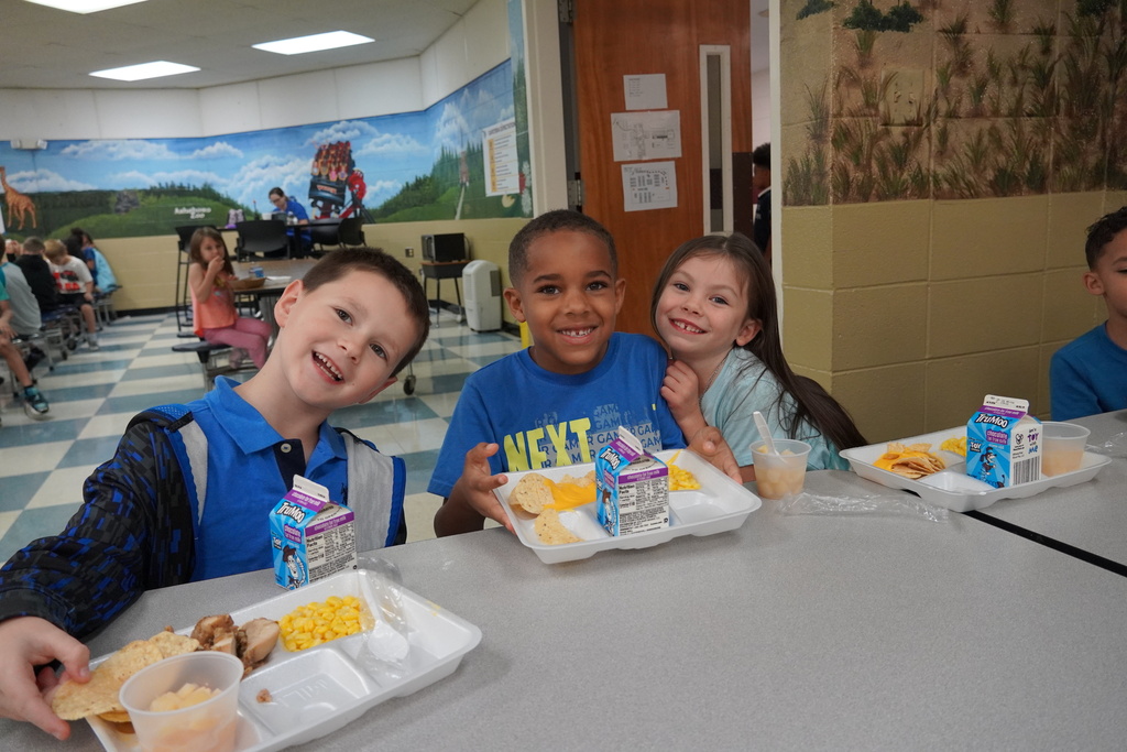 students smiling at lunch table with nachos on their tray