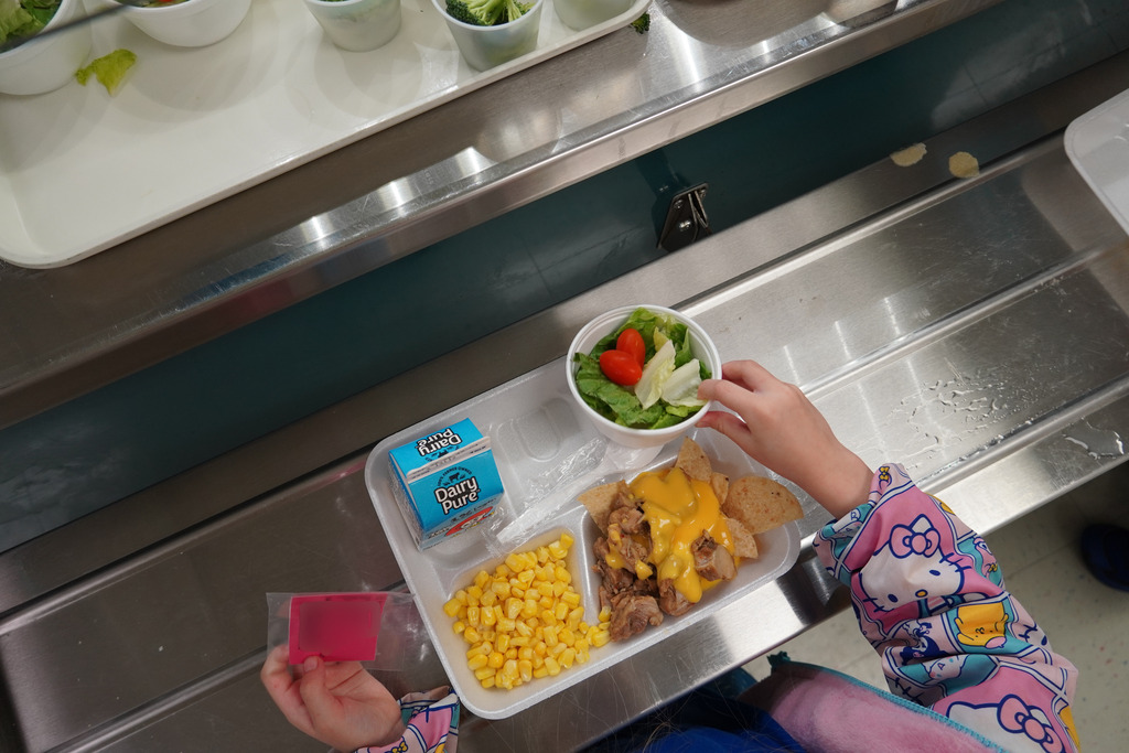 student adding salad to tray of nachos and corn
