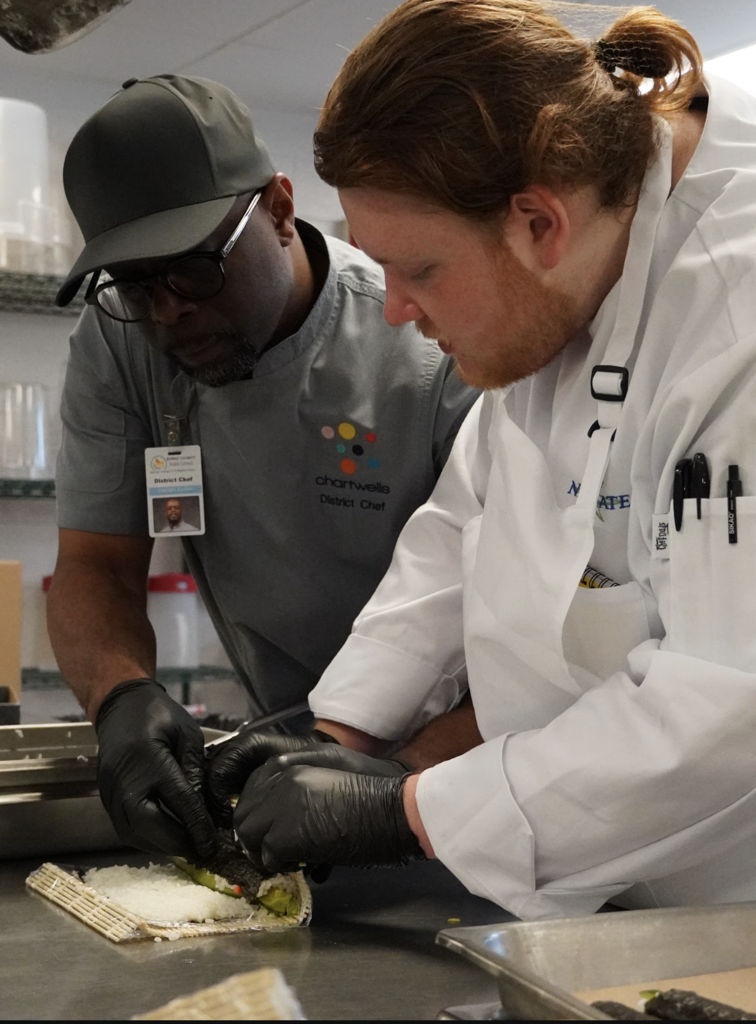 chef helping student roll a sushi roll