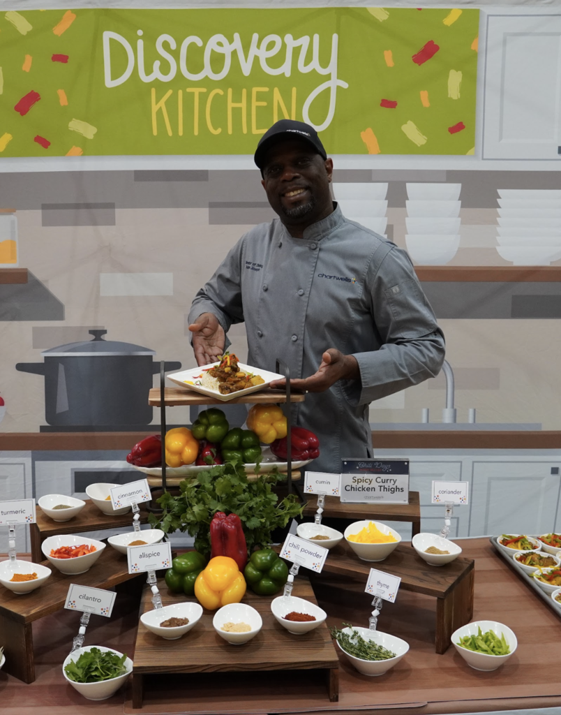 Chef posing with food for a Discovery Kitchen event with a table of spices
