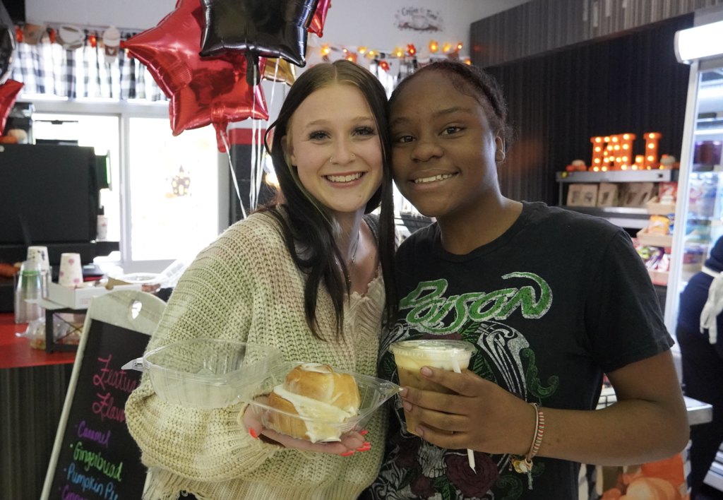 students pose with a cinnamon roll and a coffee