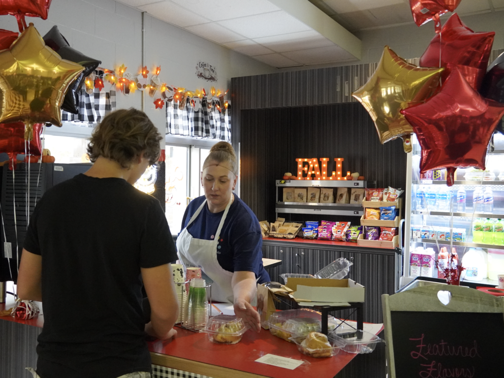 student orders at a counter at the coffee shop while worker sets out a pastry