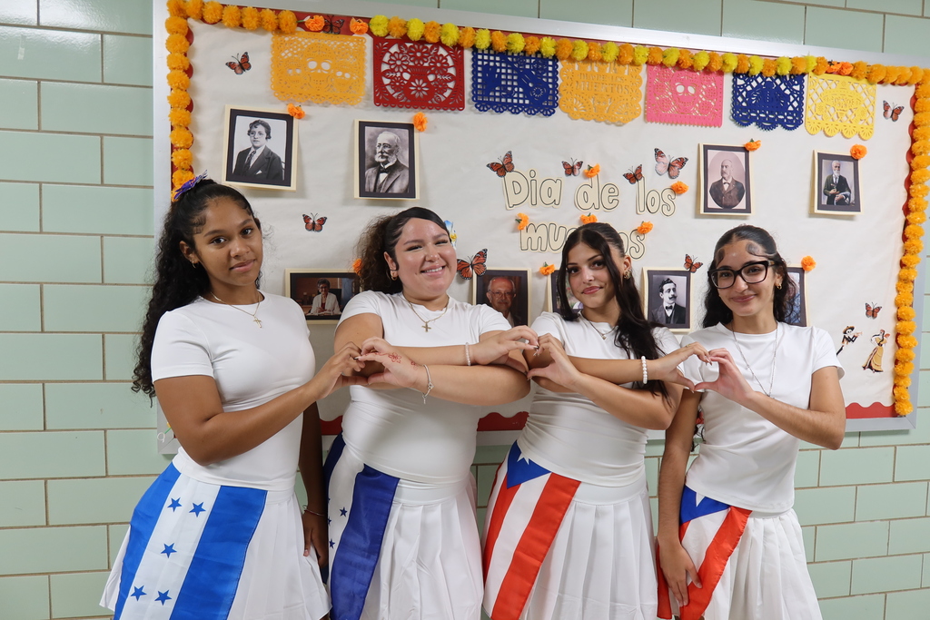 Four female students with heart hands and their flags in the hallway. 