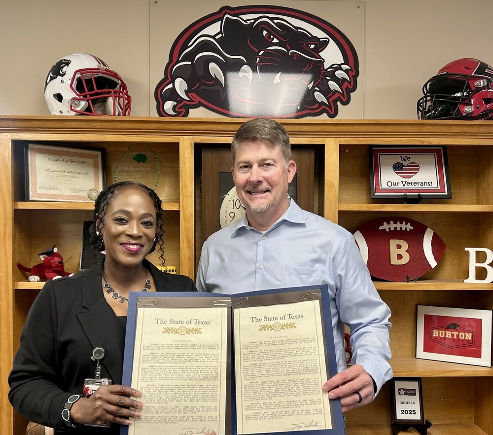 Woman and a man holding official framed declarations standing in front of a book shelf with Panther gear on it.