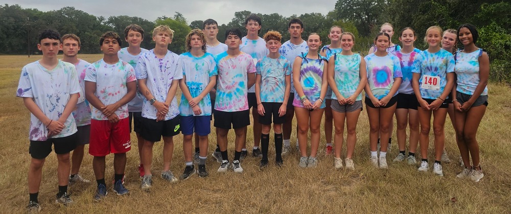 Group of students wearing tie dye shirts standing in a field.