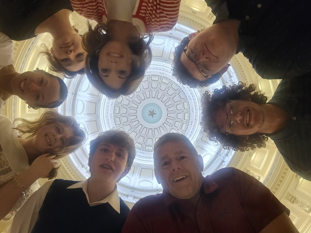 group of people looking down at camera with capitol rotunda in the background.