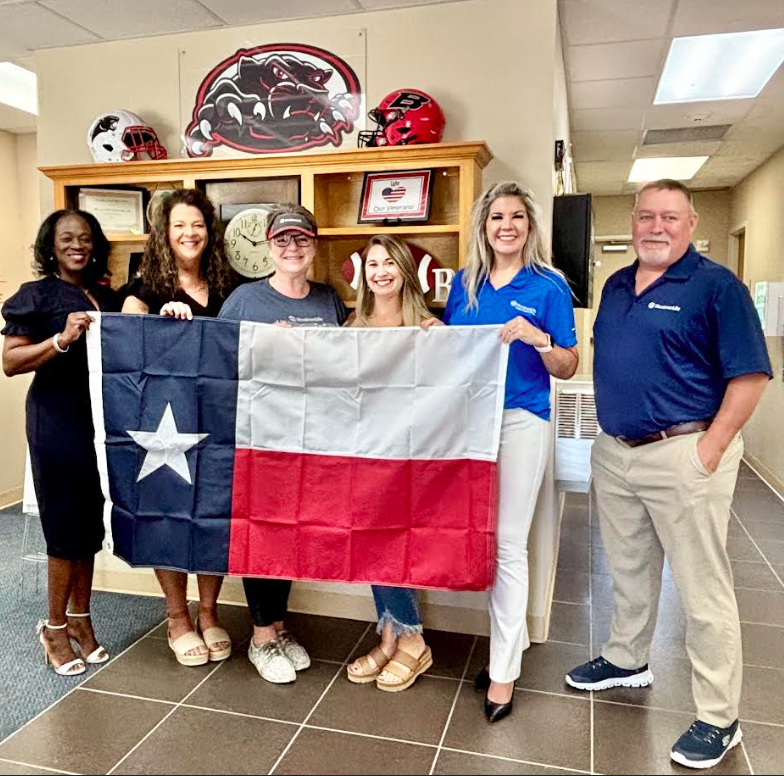 6 smiling people holding up a Texas flag
