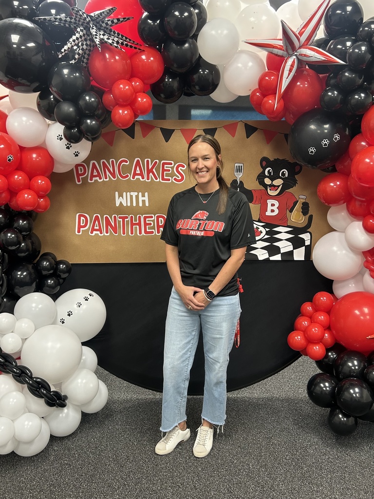 Woman in jeans and black t-shirt standing in front of colorful  balloon arrangement and banner saying Pancakes with Panthers!